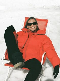 a woman laying on top of a snow covered ground next to a red lawn chair