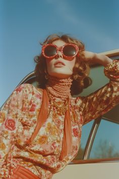 a woman wearing sunglasses leaning on the back of a car