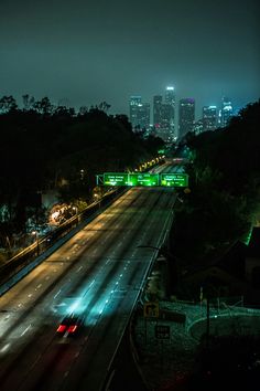 the city skyline is lit up at night, with cars driving down the road in the foreground