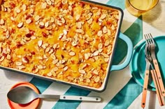 a casserole dish with almonds and orange sauce on a tablecloth next to utensils