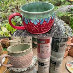 several cups and mugs are stacked on top of each other in front of some plants