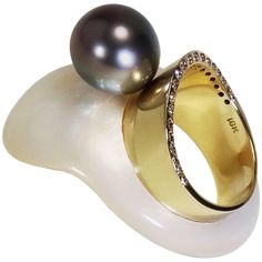 Hand carved mother of pearl with 18K gold band inlaid. Wearable sculpture on your finger, featured a 12 mm Tahitian pearl sitting on top of an 18K gold band measured 9 mm, accented with round brilliant cut diamonds 0.20 TCW set onto the side half way around the band. The interior diameter of the ring measured 17.5 mm, Size 7.25 US Finished: polished Wearable Sculpture, Shell Ring, Tahitian Pearls, Mother Pearl, Tahiti, Gold Band, Round Brilliant Cut Diamond, Gold Bands, Fashion Rings