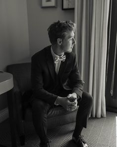 a man in a suit and bow tie sitting on a couch looking out the window