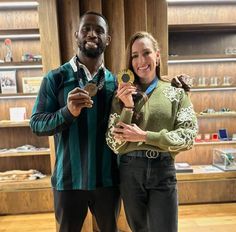 a man and woman standing next to each other holding medals