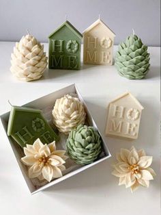 small green and white decorations in a box on a table with pine cones, house shaped candles and flowers