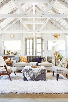 a living room filled with lots of furniture next to a white ceiling covered in wooden beams