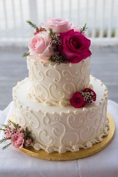 a three tiered wedding cake with pink and red flowers on the top, sitting on a table