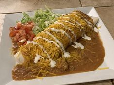 a white plate topped with enchilada covered in gravy and cheese