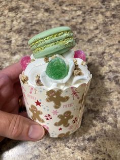 a hand is holding a cupcake decorated with green and white frosting on it