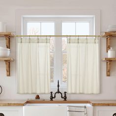 a kitchen with a sink, dishwasher and window covered in white drapes