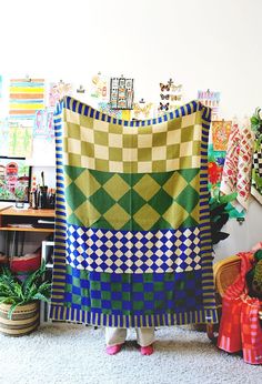 a woman standing in front of a colorful quilt on the floor next to potted plants