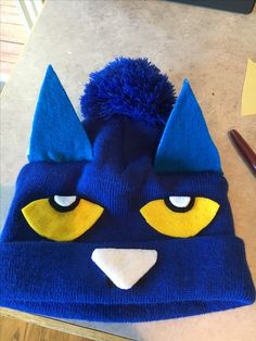 a blue knitted hat with yellow eyes and ears on top of a wooden table