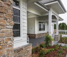 the front porch of a house with stone pillars and columns on each side, along with landscaping