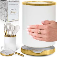 a woman's hand holding onto a white and gold container with utensils in it