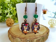 a pair of owl earrings sitting on top of a wooden stump next to a potted plant