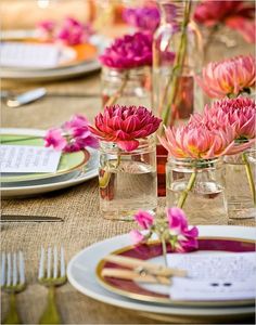 the table is set with pink flowers in mason jars and place settings for dinner guests