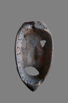 an old mask with holes in it on a gray background, worn out and rusted