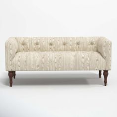 an upholstered couch with wooden legs and buttons on the back, against a white background