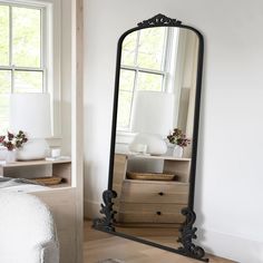 a large gold framed mirror sitting on top of a wooden floor next to a bed