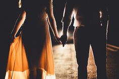 a man and woman holding hands while walking down the street in the dark at night