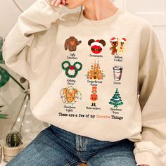 a woman sitting on a chair wearing a white sweatshirt with mickey mouses and christmas trees