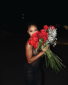 a woman holding flowers in her hands and posing for the camera on a dark street