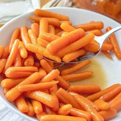 a spoon full of baby carrots sitting in a white bowl on top of a table