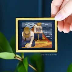 a person holding up a cross stitch picture