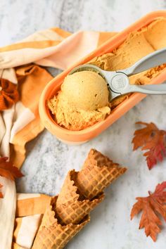 two scoops of ice cream in an orange container with autumn leaves around it and on the table