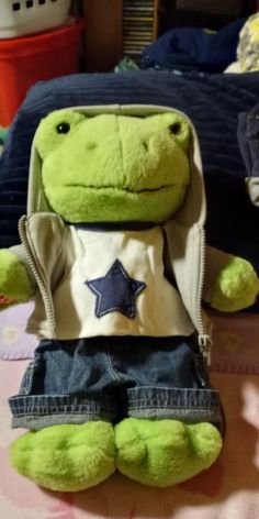 a green stuffed animal sitting on top of a bed next to a blue and white pillow