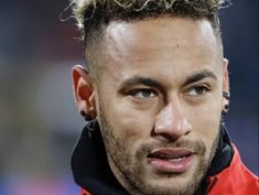 a close up of a soccer player wearing a red jacket and ear piercings on his ears