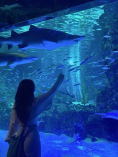 a woman standing in front of an aquarium looking at sharks