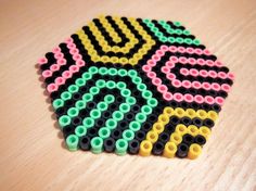 a close up of some sort of bead pattern on a wooden surface with black, yellow, green and pink beads