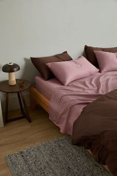 a bed with pink and brown sheets in a bedroom next to a night stand on a wooden floor