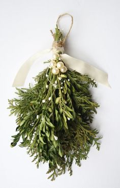 a bunch of green plants hanging from a white ribbon on top of a wall ornament