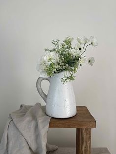 a white vase with some flowers in it on a wooden table next to a blanket