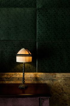 a lamp sitting on top of a wooden table next to a green wall and purple chair