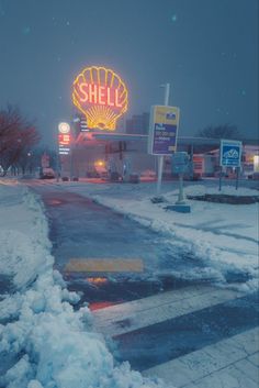 a snow covered street next to a shell gas station