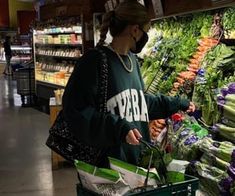 a woman wearing a face mask shopping in a grocery store with vegetables and other groceries