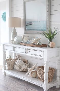 a white console table with sea shells on it and a mirror over the sideboard