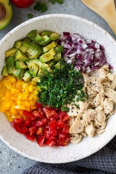 a white bowl filled with chopped vegetables next to an avocado and tomato slice