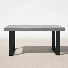 a concrete table sitting on top of a cement floor next to a white wall with black metal legs