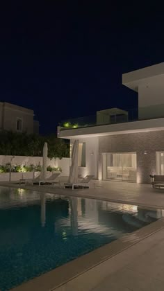 an empty swimming pool in front of a modern house at night with the lights on