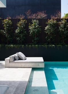 an outdoor lounge chair next to a swimming pool with plants on the wall behind it