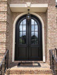 a black double door with arched glass and wrought iron railings on a brick building