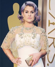 a woman in a white dress with purple hair and gold accessories on the red carpet