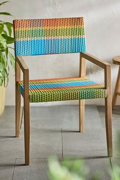 a colorful chair sitting on top of a cement floor next to a potted plant