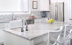 a kitchen with marble counter tops and white chairs in front of an island that has two lemons on it