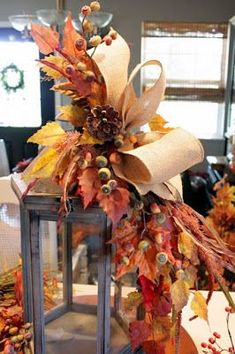 a lantern is decorated with fall leaves and burlucks for the centerpiece