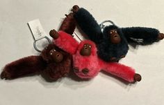 three monkey keychains are sitting on a white surface, one is red and the other is black